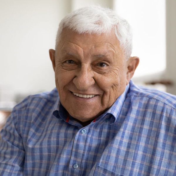 A senior man in a blue button-down shirt and white hair smiles at the camera.