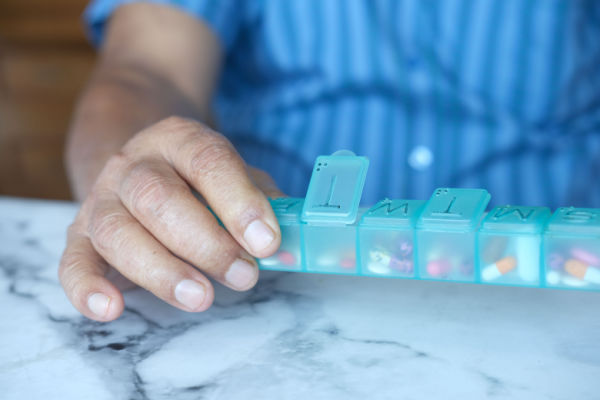 An adult holds a pill box with medications in each section. Each section is labeled with the first letter of the day of the week. 