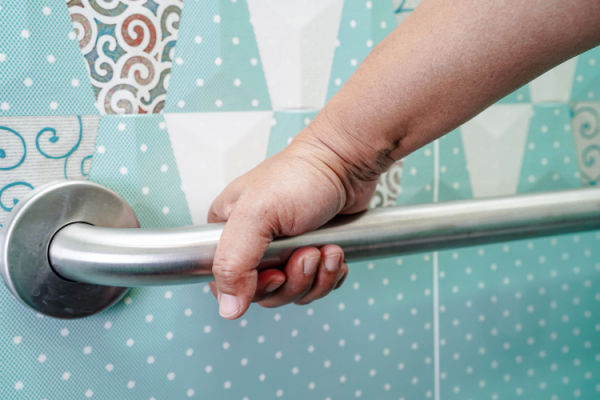 A hand grasps a grab bar in a bathroom. 