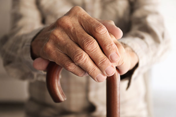 An elderly person's hands grip the top of a cane. 