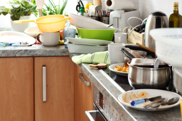 A kitchen with piles of dirty dishes in the sink and on the counter. 