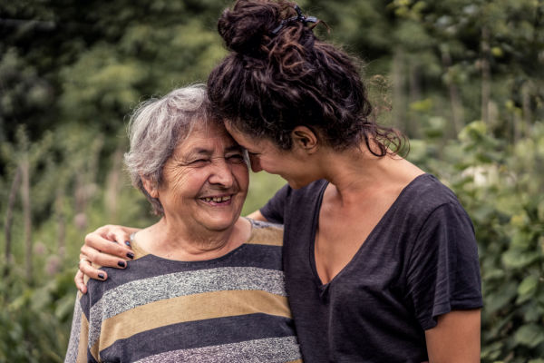 An older woman and younger woman, perhaps smother and daughter, smile widely as they gently hug. 