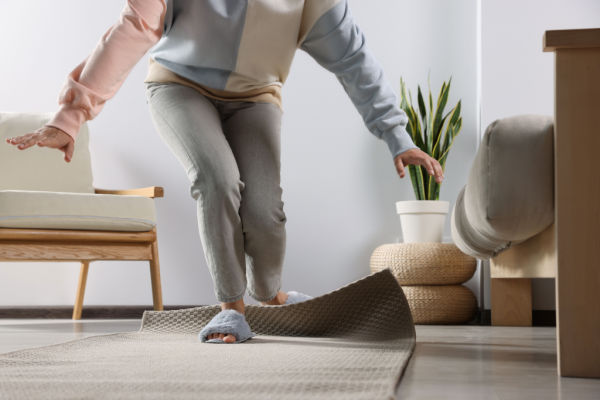 A woman wearing slippers is starting to trip over the edge of a loose carpet. 