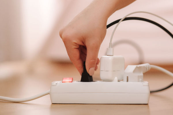 A woman's hand holds a plug that's plugged into a power strip. A couple of other things are plugged in as well. 