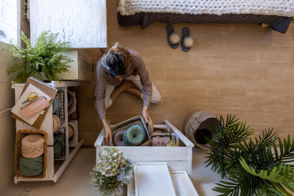 An aerial view of a woman sitting on the floor while she organizes the contents of a yarn drawer. 