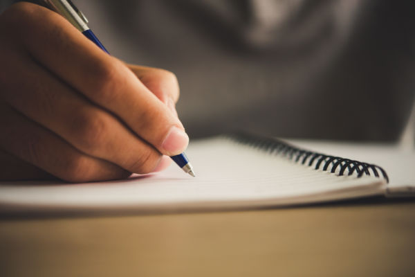 A close-up of a hand holding a pen as it writes in a notebook. 