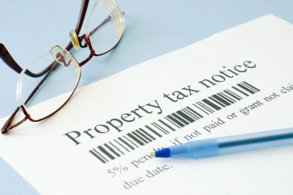 
A pair of reading glasses and a pen sitting on a piece of paper that says "Property tax notice: 5% penalty if not paid or grant not claimed by due date."