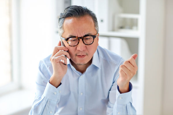 A man with glasses and a button-down shirt talks on a cell phone. He has a serious and focused look on his face. 
