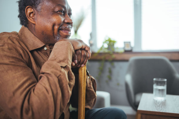 A senior man smiles with his mouth and his eyes as he rests his chin and hands on his cane.