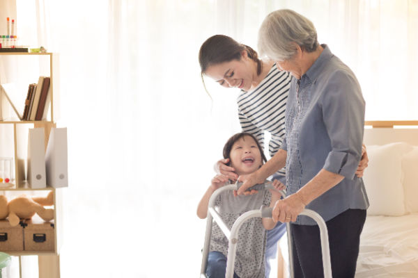 An older woman, a middle aged woman, and a child all smile and laugh together as the older woman gently rests on a walker. 