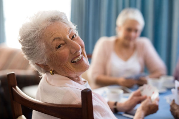 An older woman gives a big smile during a card game with another older woman. 