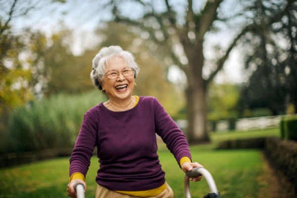 A senior woman smiles widely as she walks with the support of her walker. 