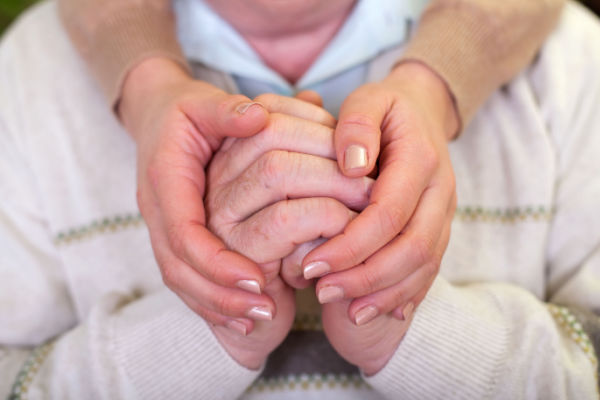 A pair of senior hands are being lovingly cupped by the hands of someone younger.