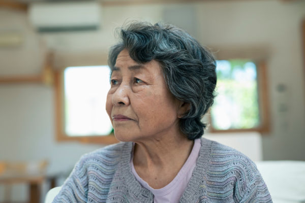 An older Asian woman in a sweater looks to the side with a sad, worried, or anxious look on her face. 