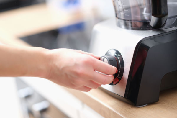 A woman turns the knob of a blender. 