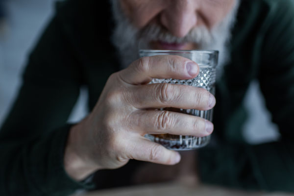 A senior man with a mustache and beard holds a glass containing alcohol. 