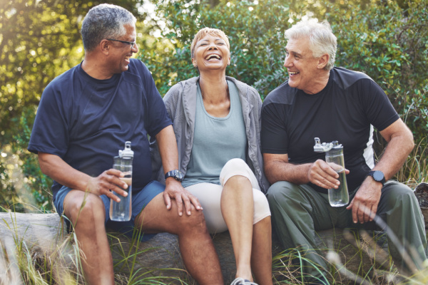 Three senior adults sit together outside and have a laugh while taking a break from exercise. 