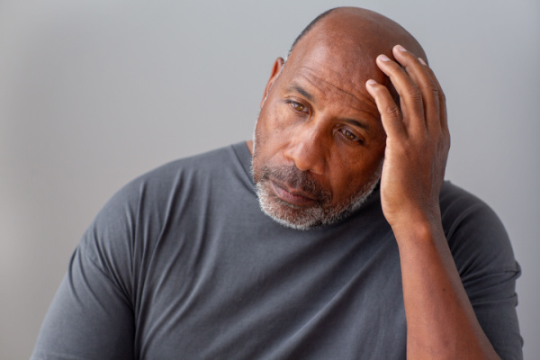 A senior man worriedly looks down as he holds his hand to his head.