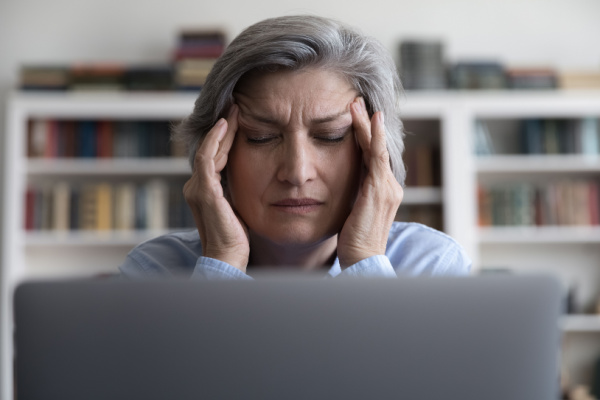 A senior woman has one hand on each temple as she closes her eyes.