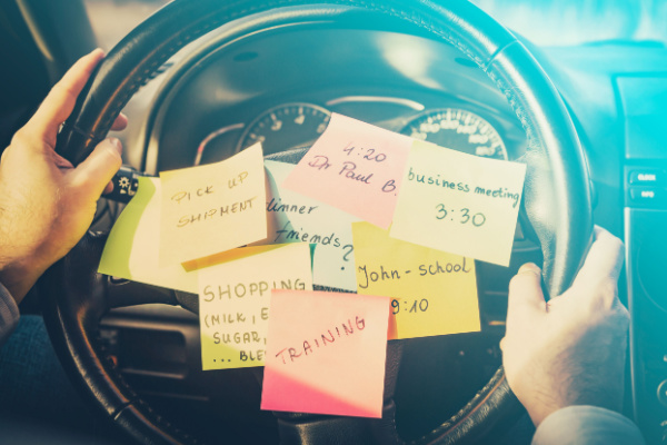 A steering wheel with multiple Post-It notes listing out different tasks, responsibilities, and to-dos. 