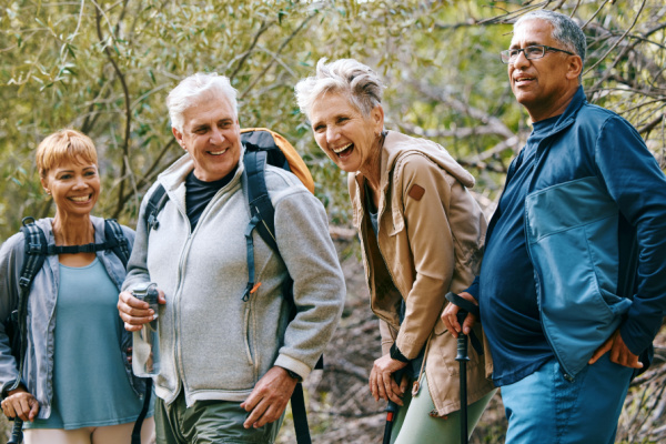 A group of seniors smiles and laughs while hiking in the woods.