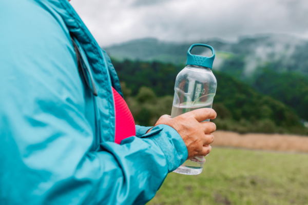 Woman holds water bottle while hiking outside.