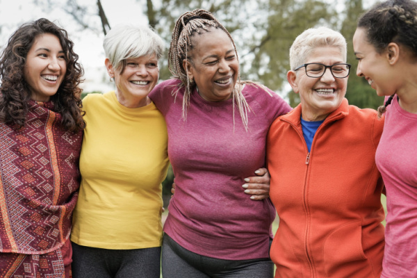 Women of various ages smile as they put their arms around each other. 