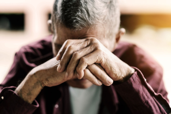 An elderly man puts his head in his hands as he looks stressed, upset, or anxious.