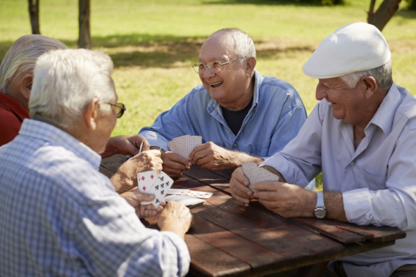 Older men smile and laugh as they play cards outside together. 