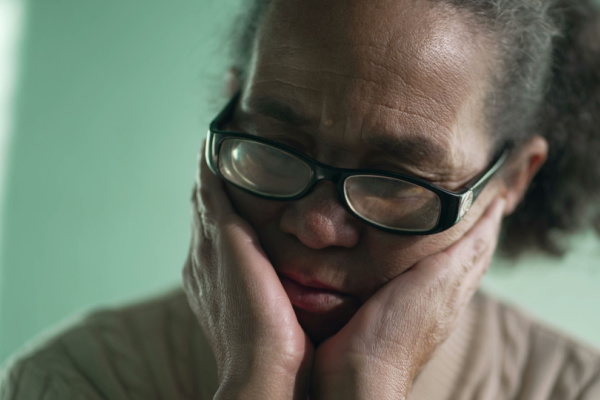 An older woman has her head in her hands as she looks anxious or sad. 