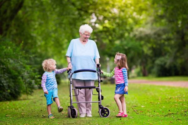 A senior woman with a walker stands next to her grandchildren.