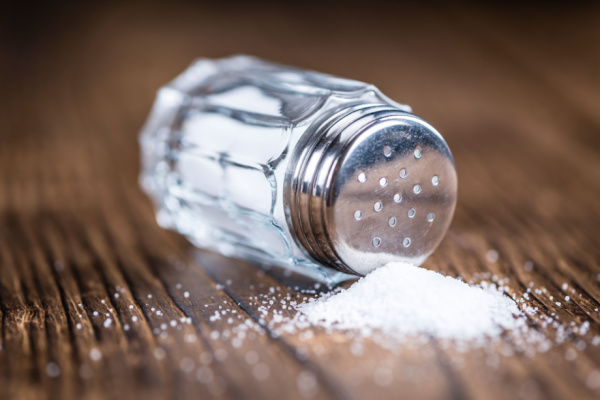 A tipped-over salt shaker with salt spilling out of it. 