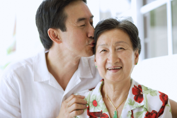 A man gently kisses the top of his senior mother's head. 