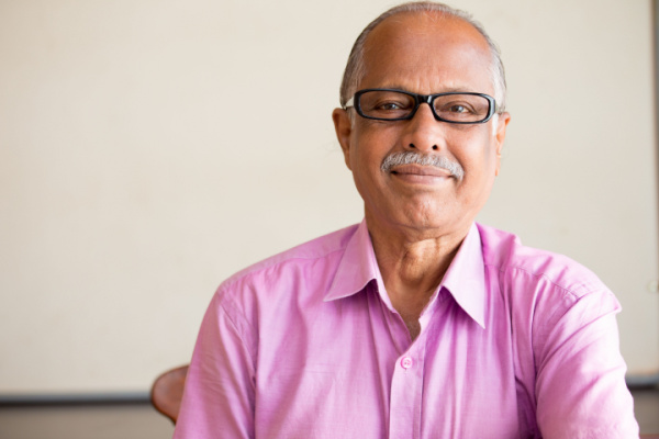 A senior man in glasses and a pink polo shirt smiles at the camera.