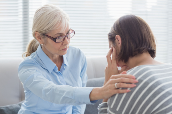 A woman puts her head in her hands as she is comforted by a therapist. 