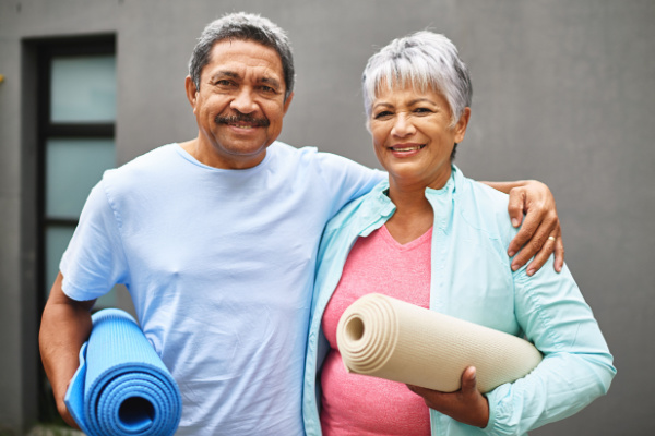 A senior man and woman smile as they hold exercise mats. 