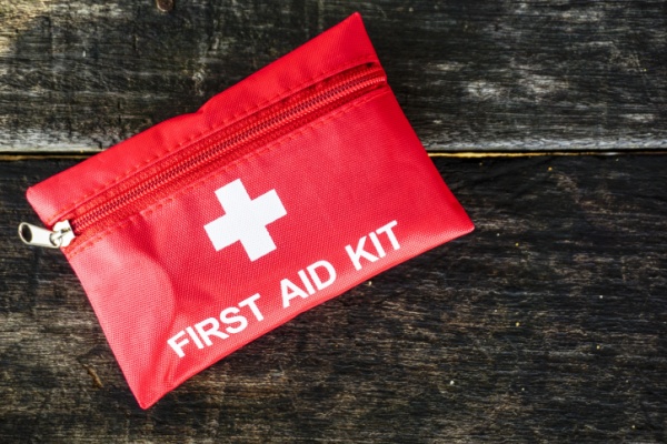 A red first aid kit sitting on a dark wood background. 