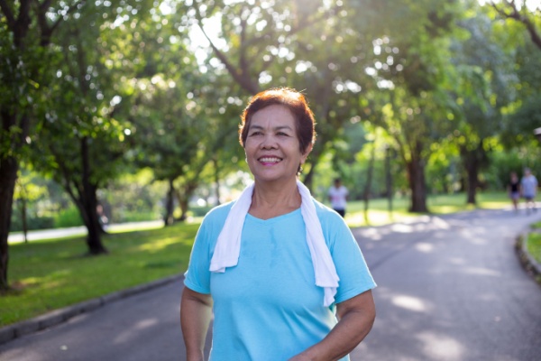 A senior woman smiles as she walks on a path outside. 