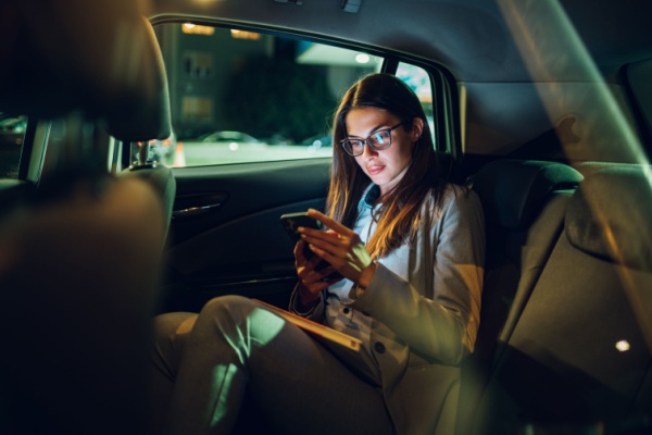A woman sits in the back seat of a car while looking at her cell phone. 
