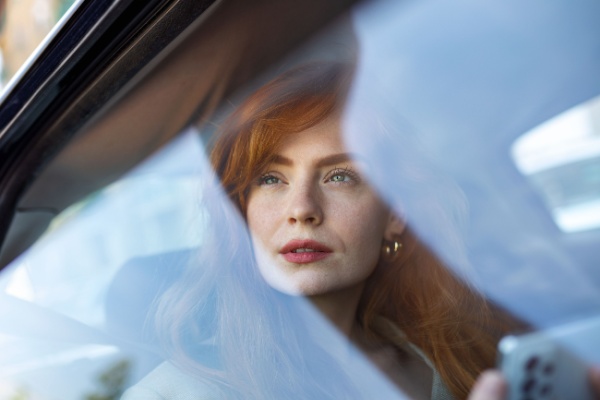 A woman looks out the backseat window of a car. 