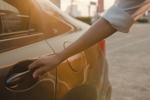 A woman's hands extends to open a passenger car door from the outside.