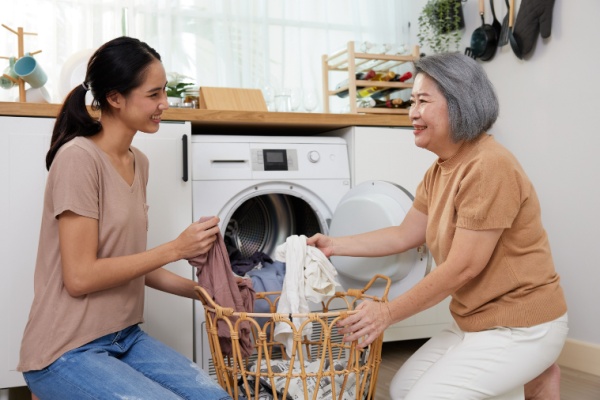 A senior woman and a younger woman fold clothes in front of a dryer.