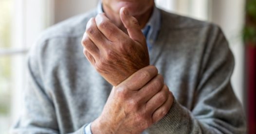 A senior man holds his wrist, which appears to be sore.