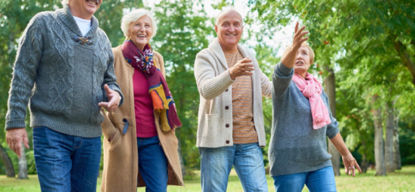 A group of seniors walk outside together. They are smiling and laughing.