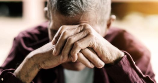An elderly man puts his head in his hands as he looks stressed, upset, or anxious.