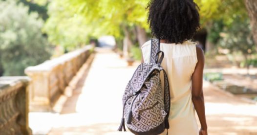 A young woman walks down the road while holding a backpack.