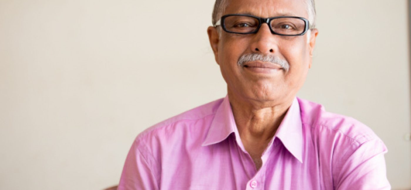 A senior man in glasses and a pink polo shirt smiles at the camera.