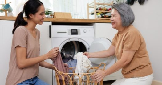 A senior woman and a younger woman fold clothes in front of a dryer.