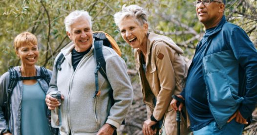 A group of seniors smiles and laughs while hiking in the woods.