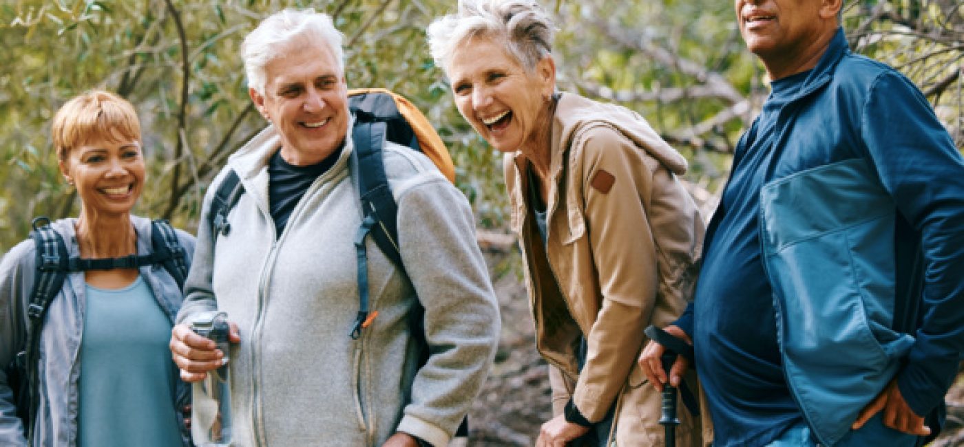 A group of seniors smiles and laughs while hiking in the woods.